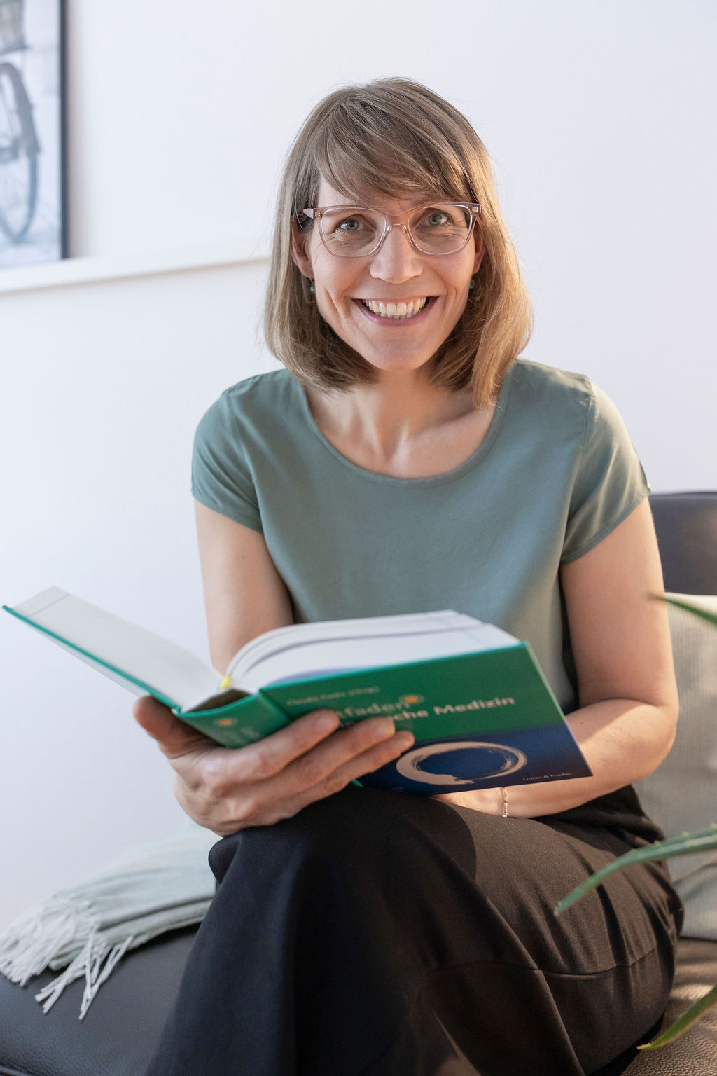 Porträt von Sonja Looser mit einem Fachbuch zur Traditionellen Chinesischen Medizin